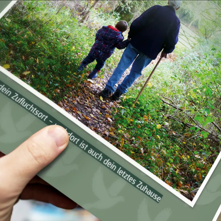 Eine Person hält ein Fotobuch in der Hand. Auf dem Cover des Fotobuchs spaziert ein Großvater mit seinem Enkel Hand in Hand durch den Wald.