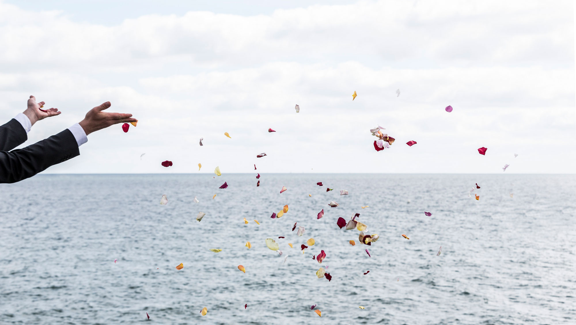 Eine Person streut Blumenblüten ins Meer.