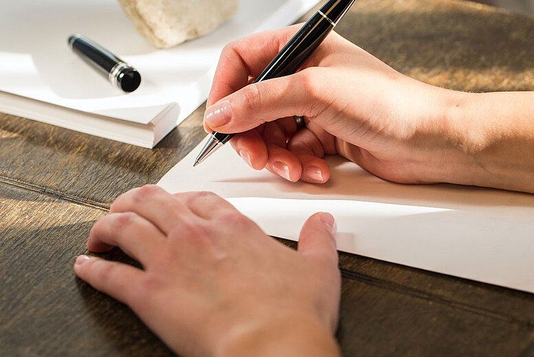 Eine Person schreibt mit einem schwarzen Stift etwas auf ein weißes Blatt Papier.