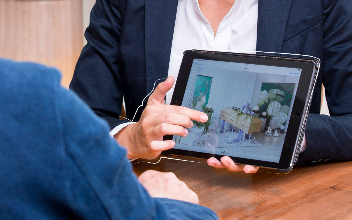 Eine Person zeigt ihrem Gegenüber etwas auf einem Tablet.